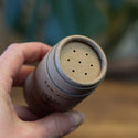 Hand holding a container of RAW ROOTS Dreadlocks Lock Powder Dry Shampoo (30g) with a close-up view of the powder dispenser holes.