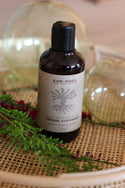 Bottle of Raw Root Herbal Cleanser on a textured surface with greenery