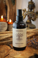 Bottle of Raw Root Rescue Tonic on a wooden surface with candles and decorative items in the background
